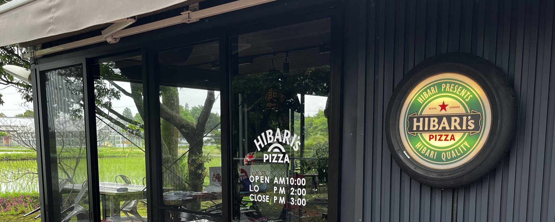 HIBARI's PIZZA & GRILL 店舗外観 — 黒ガルバの壁とタイヤ縁の看板